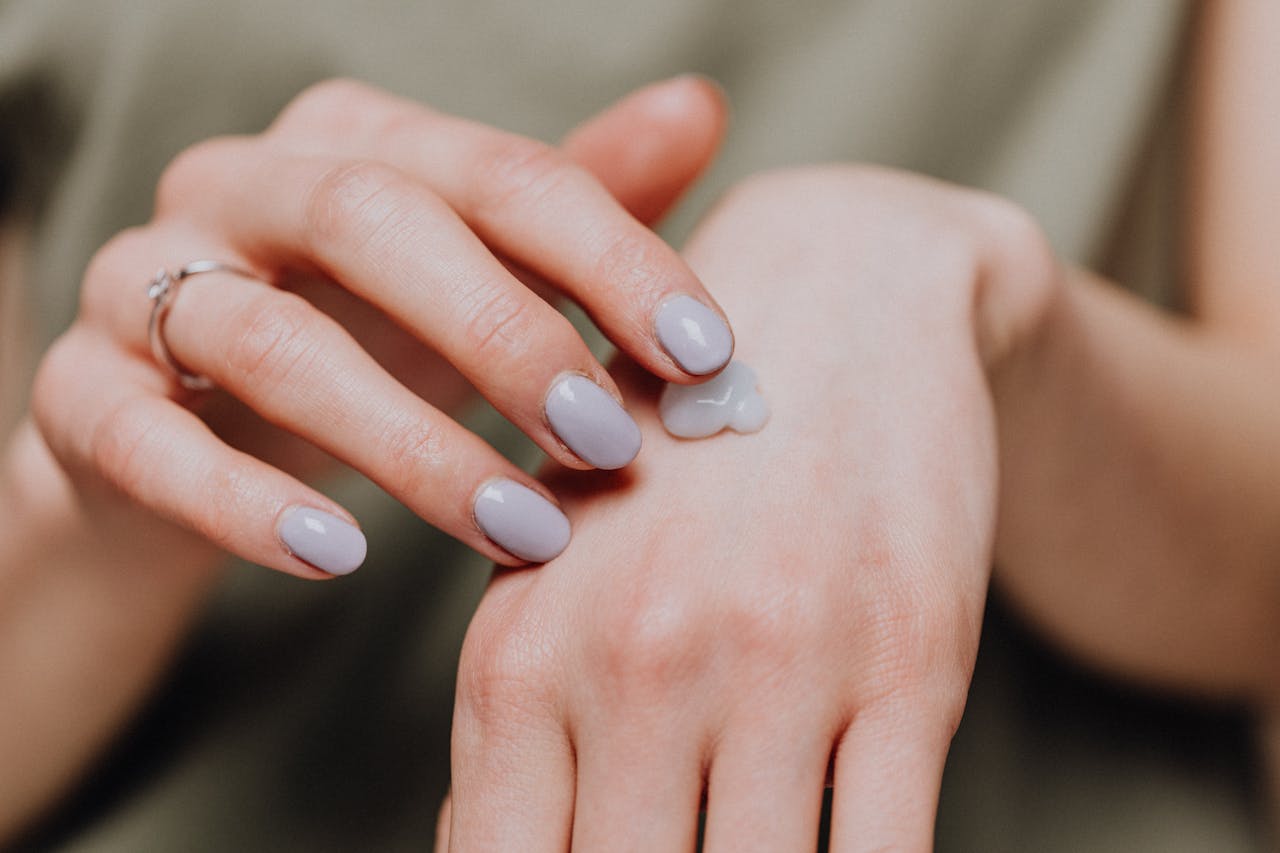 A womans hand applying moisturizing cream, emphasizing skincare and nail beauty.